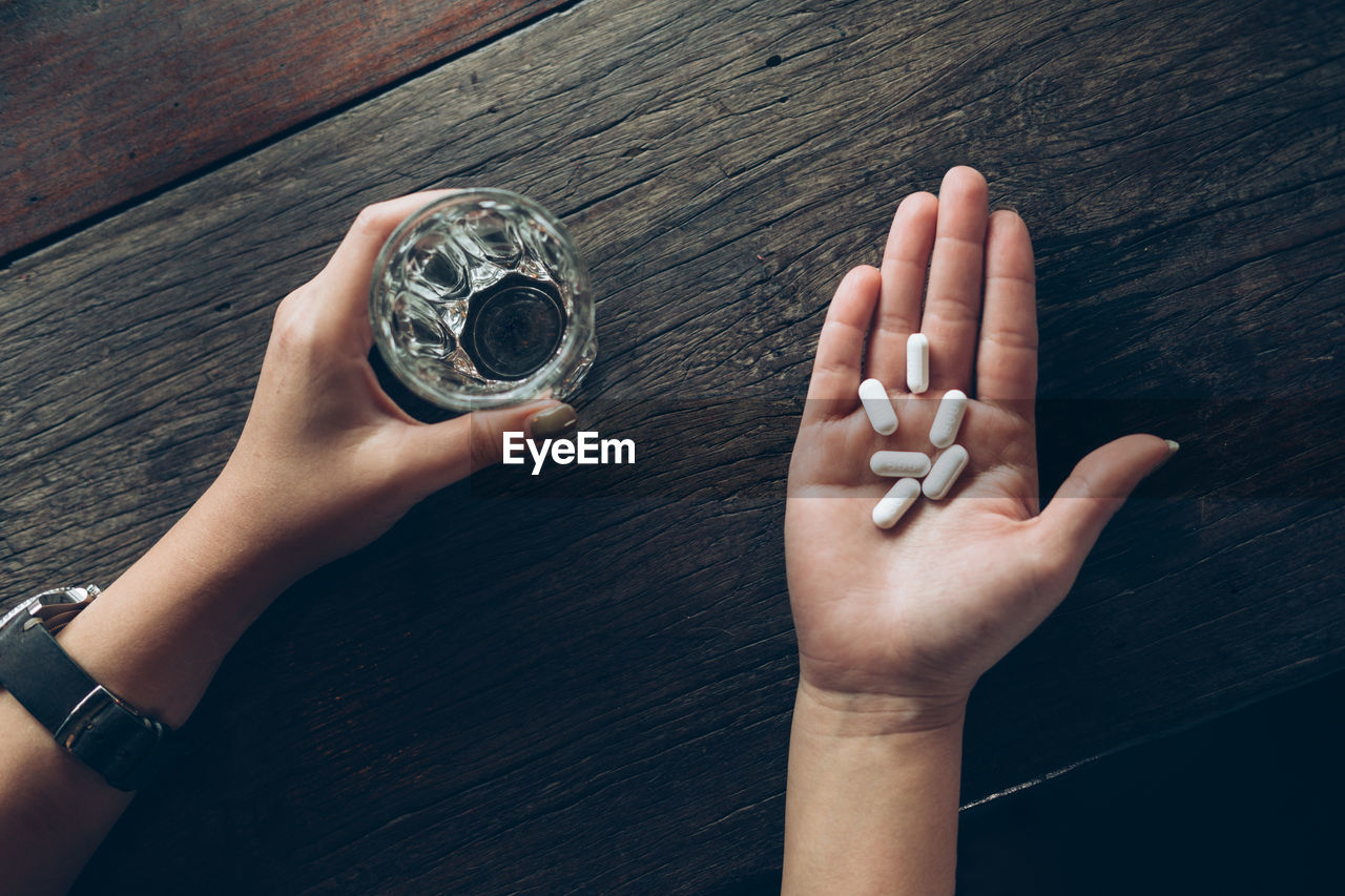Cropped hands of woman holding pills and drinking water in glass
