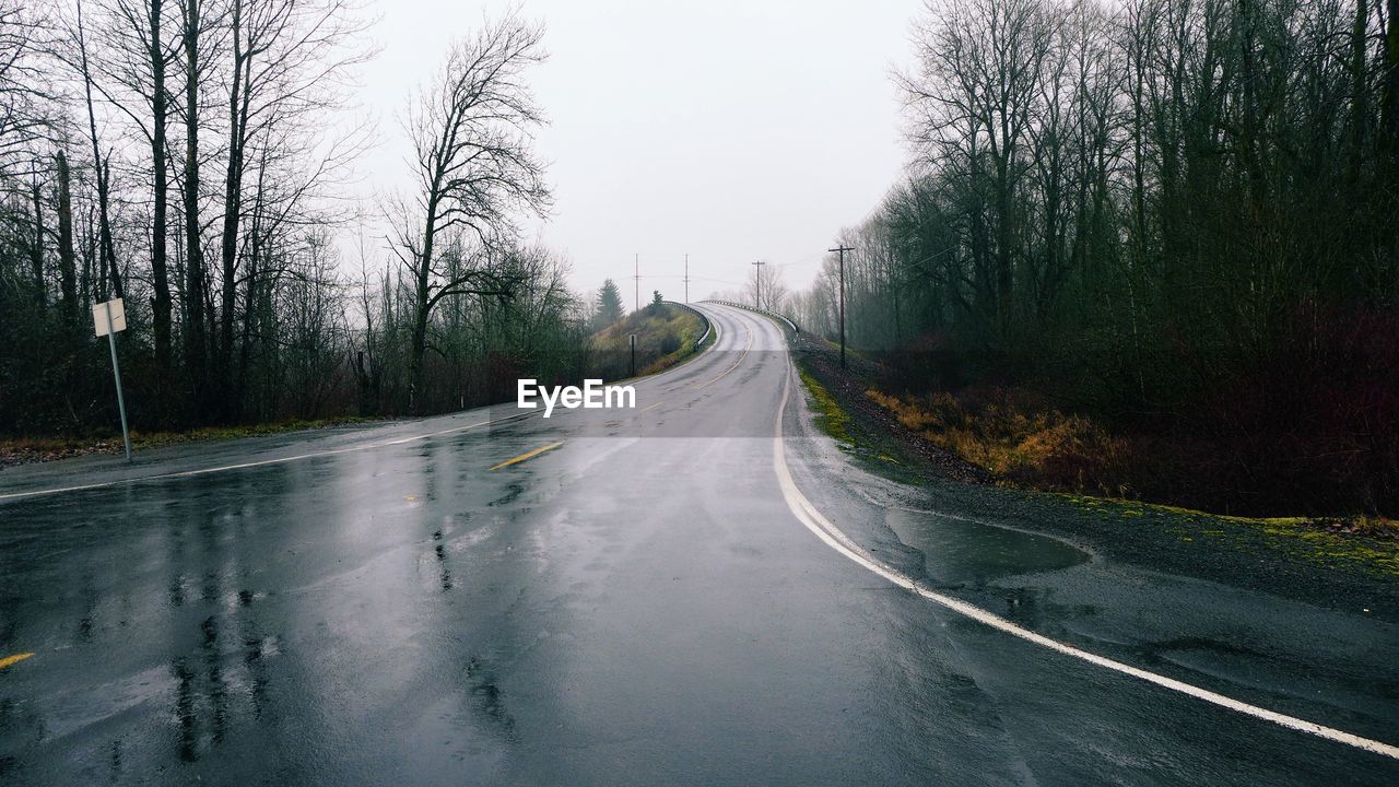 Wet empty road amidst trees against sky