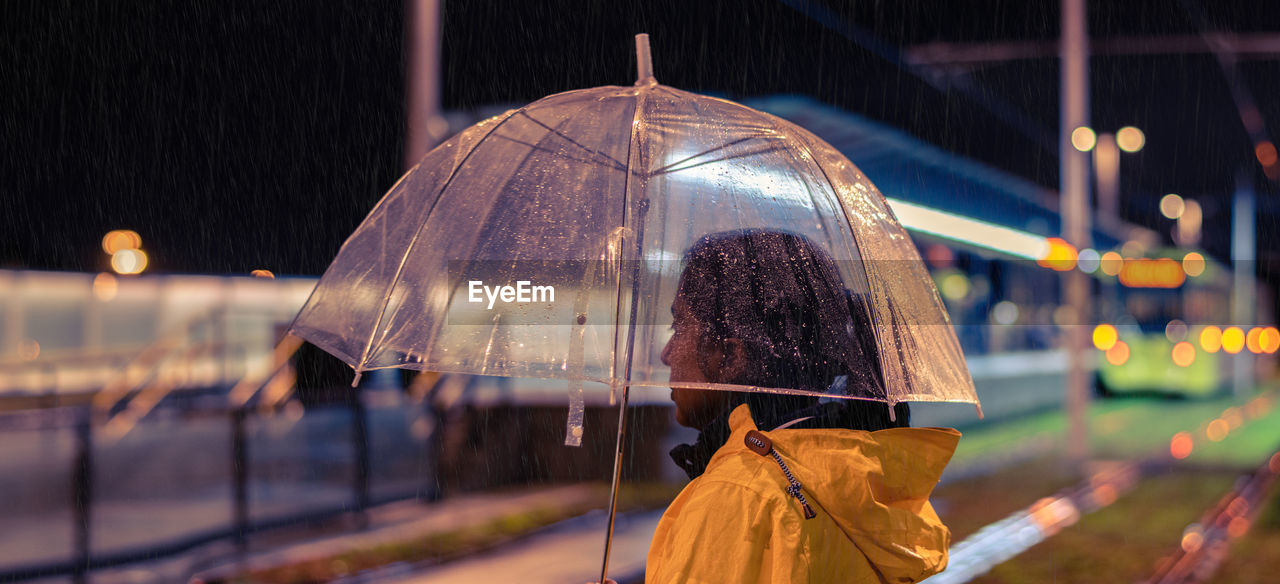 Side view of woman standing with umbrella in city at night