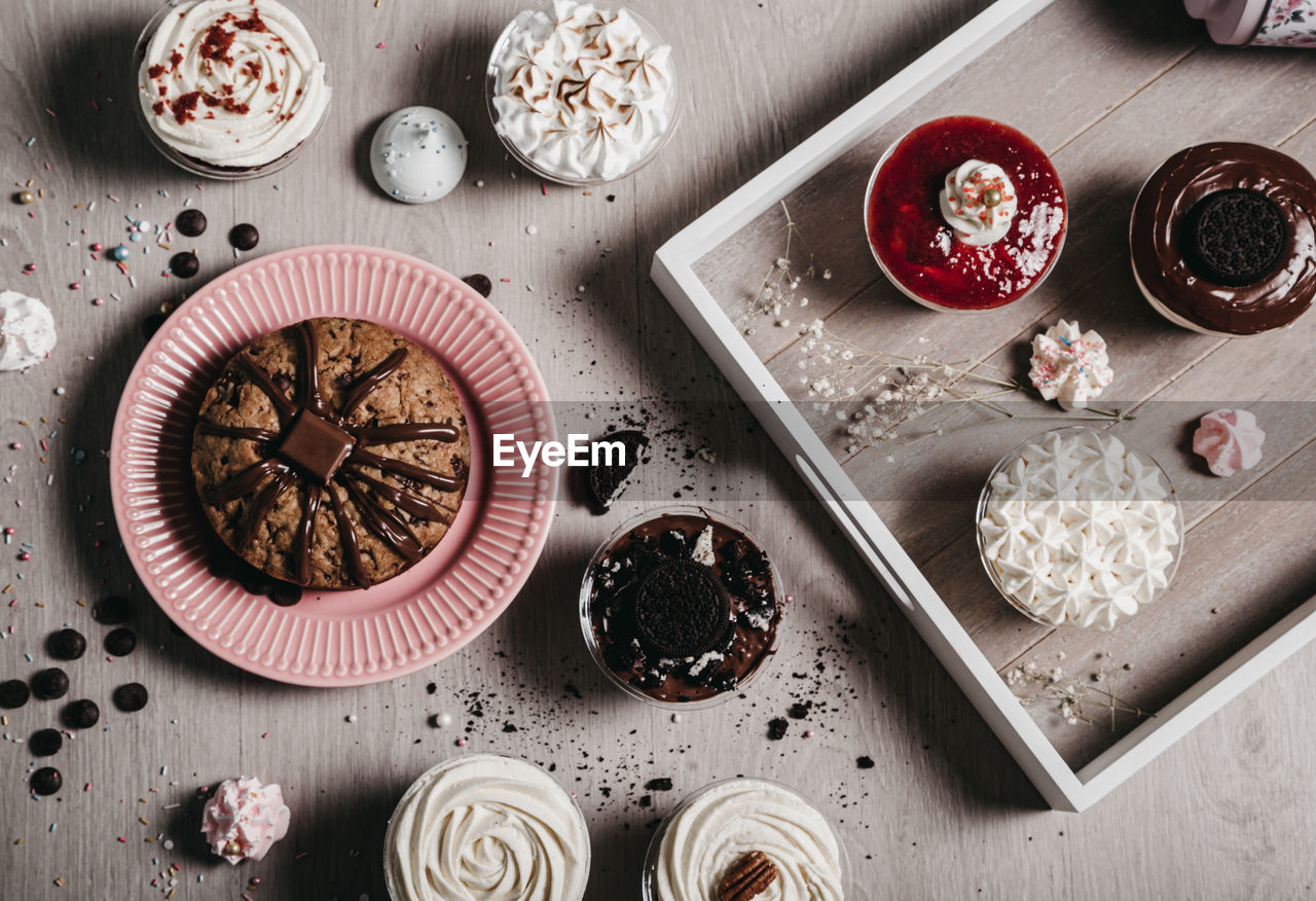 From above of chocolate cake and meringue cookies placed on table with desserts with whipped cream