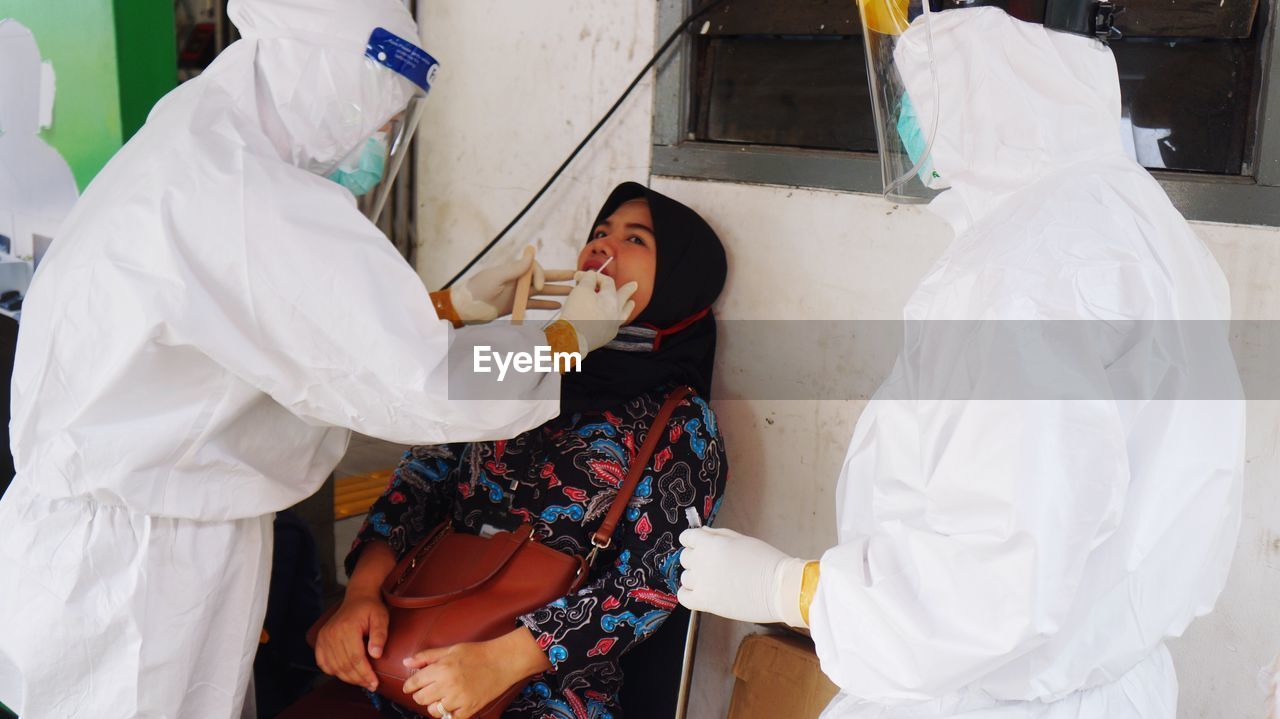 Doctors wearing protective suit examining patient while sitting outdoors