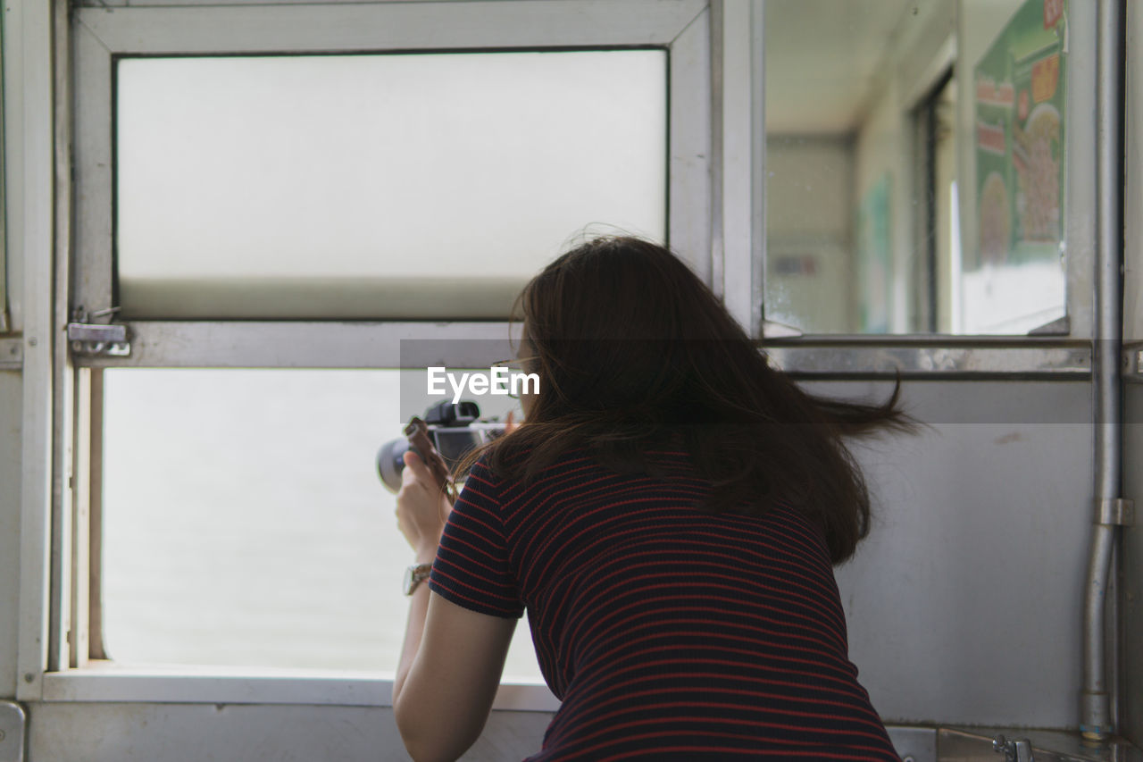 Rear view of woman photographing through window at home