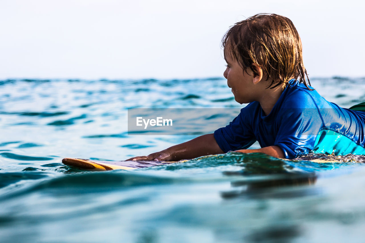 Side view of a 3 years old surfer on wooden surfboard