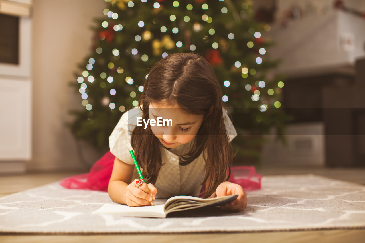 Full length of girl at christmas tree at home