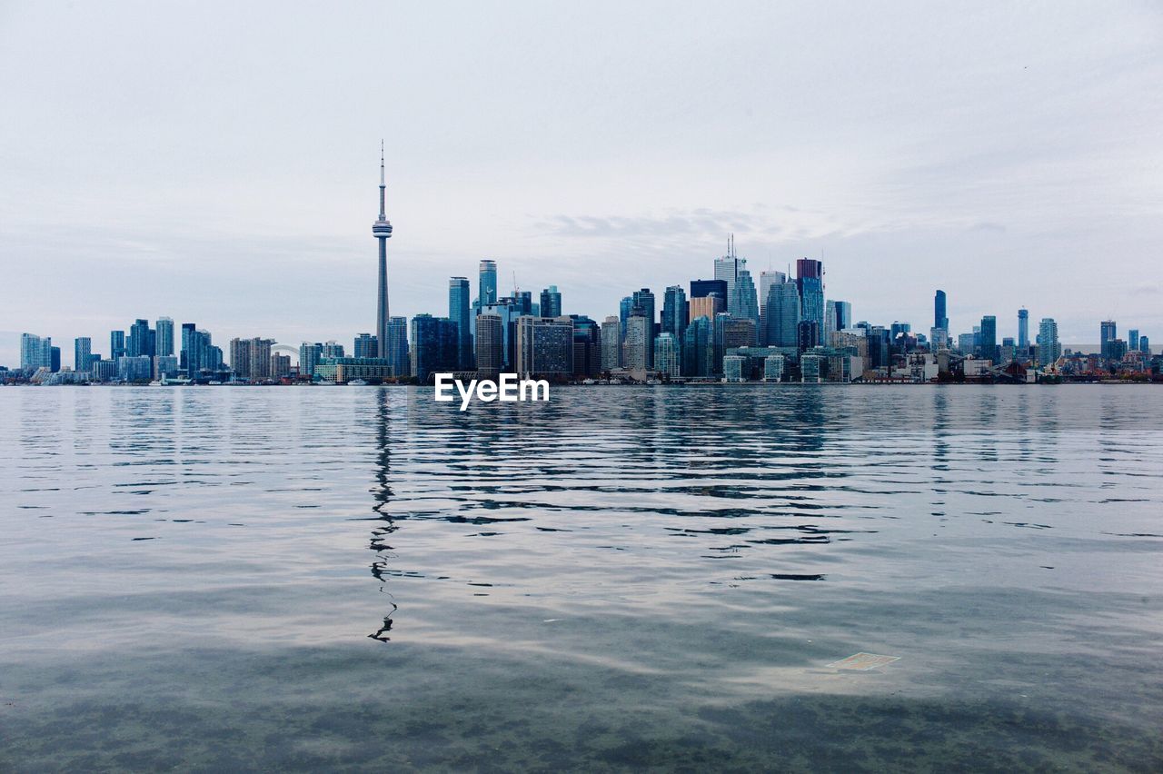 Cn tower with cityscape by river against sky