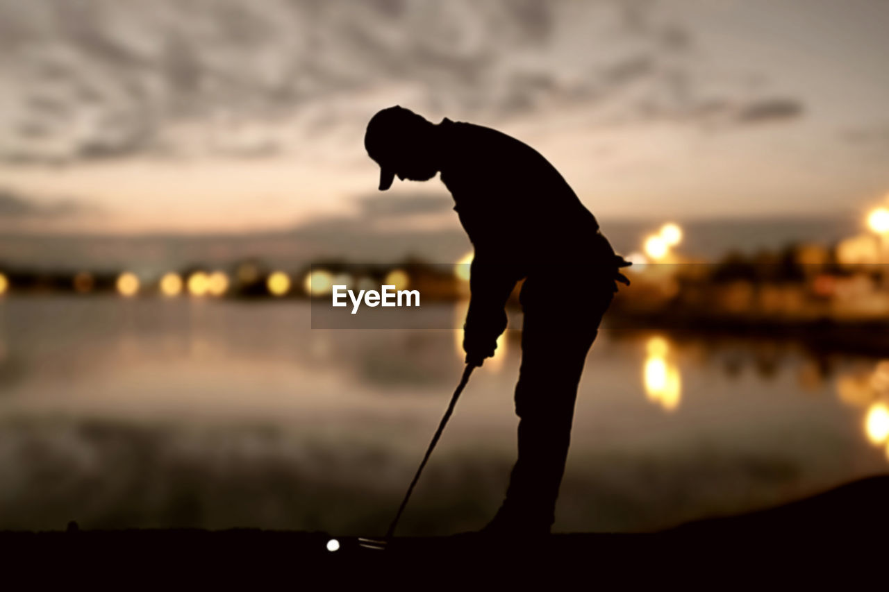 Silhouette man playing golf at sunset