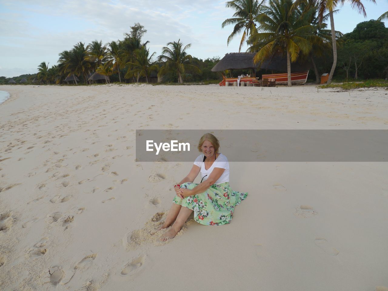 Portrait of smiling woman sitting at beach against trees