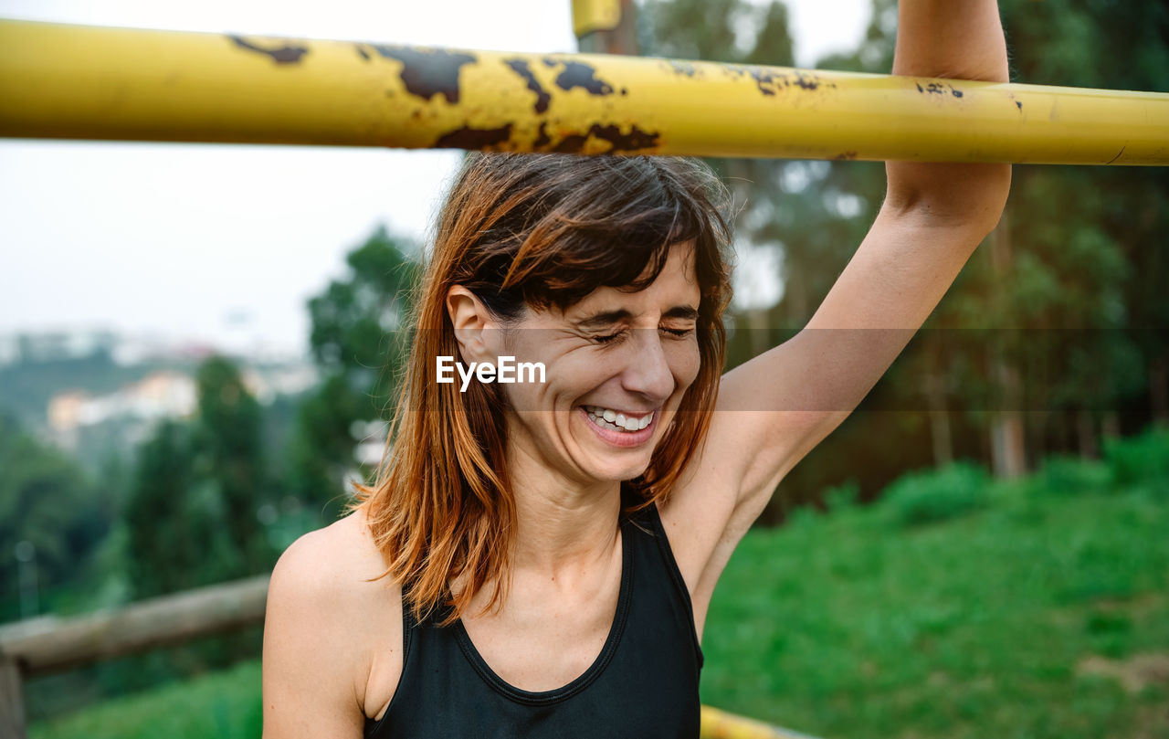 Woman with eyes closed laughing by rod against trees