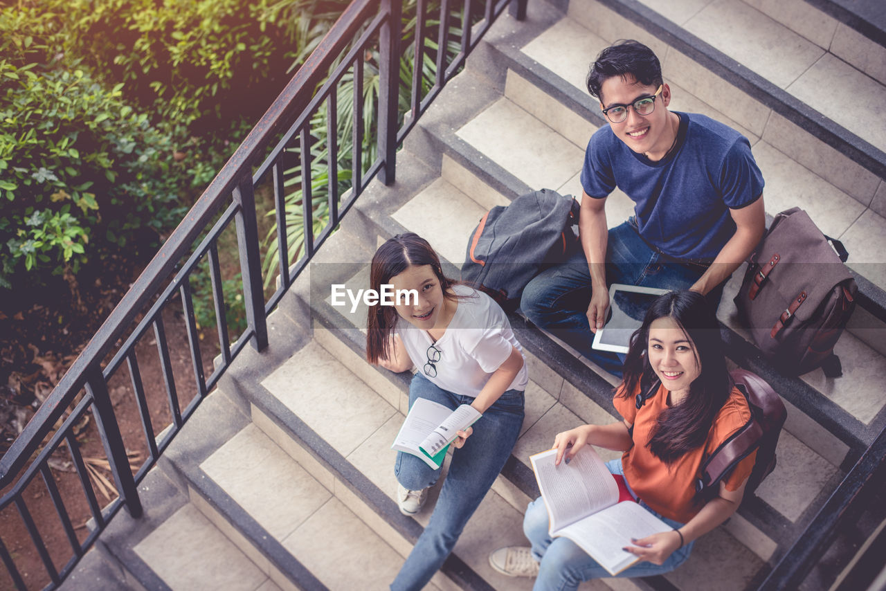 High angle portrait of friends studying while sitting on steps