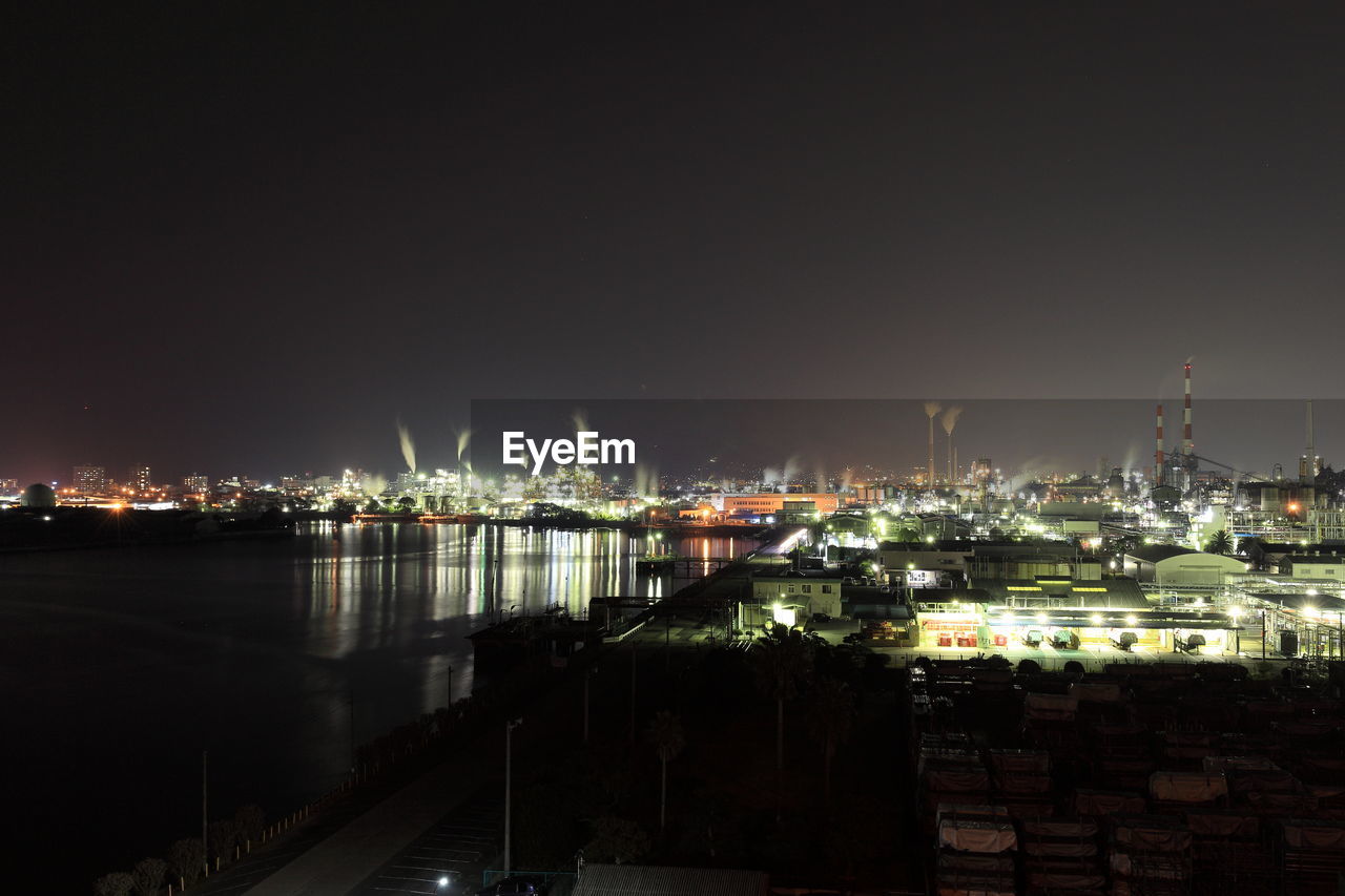 Illuminated cityscape by sea against clear sky at night