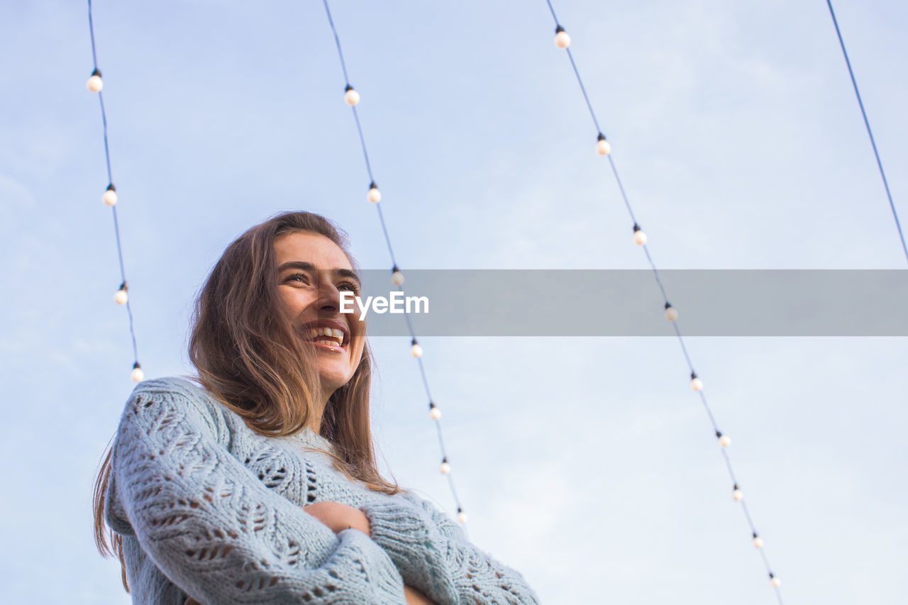 Low angle view of smiling woman looking away while standing against sky