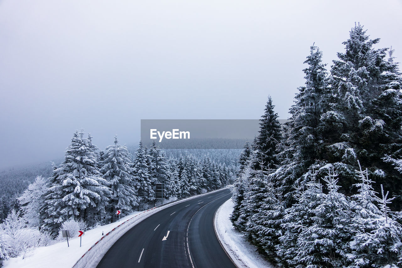 SNOW COVERED ROAD AMIDST TREES AGAINST SKY DURING WINTER