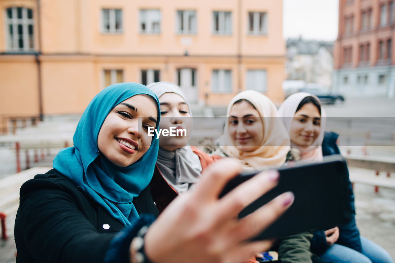 Young woman taking selfie with muslim female friends in city