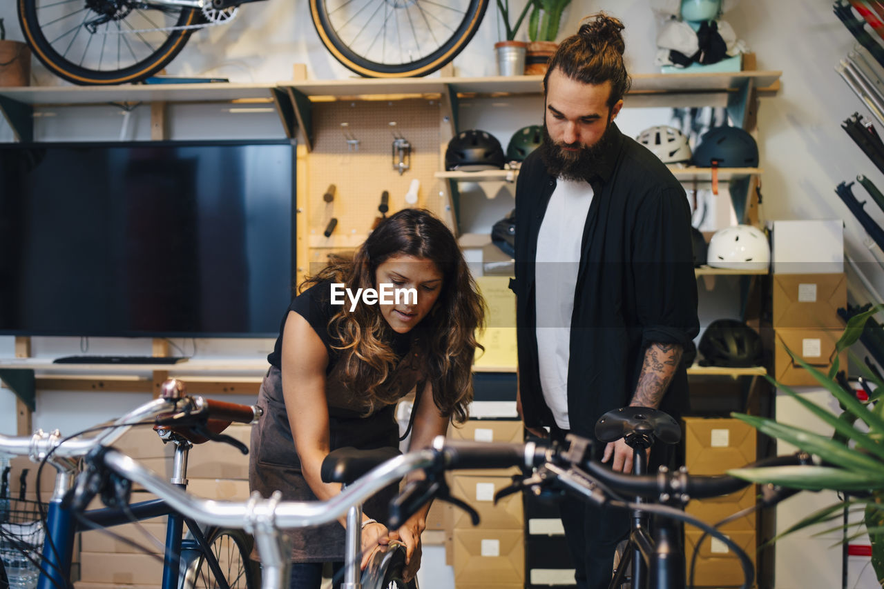 Female owner explaining about bicycle to male customer at retail store