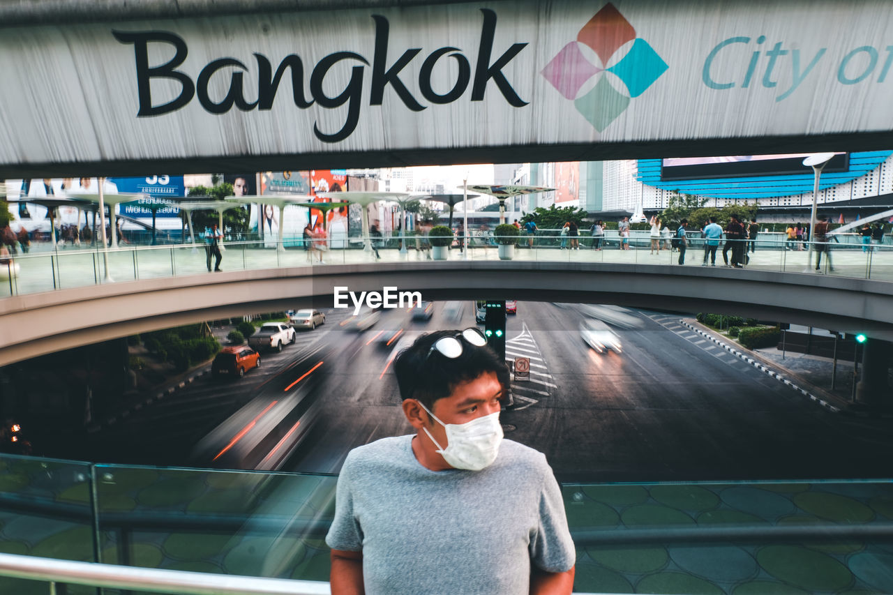 Mid adult man wearing flu mask while standing on footbridge over road in city