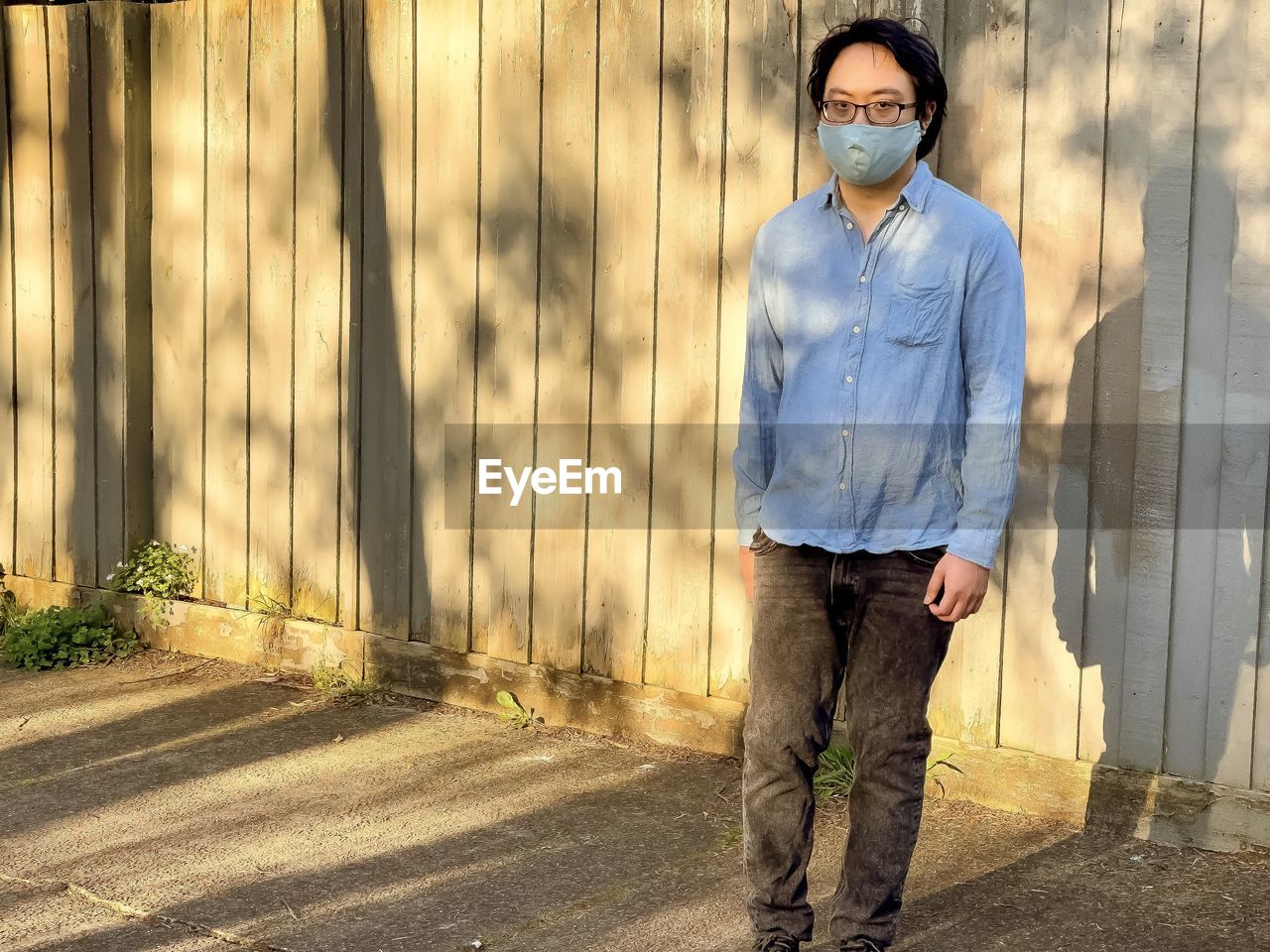 Portrait of young man wearing eyeglasses and face mask standing outdoors.