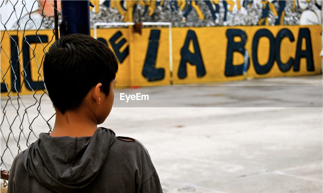 REAR VIEW OF BOY STANDING BY TEXT ON WALL