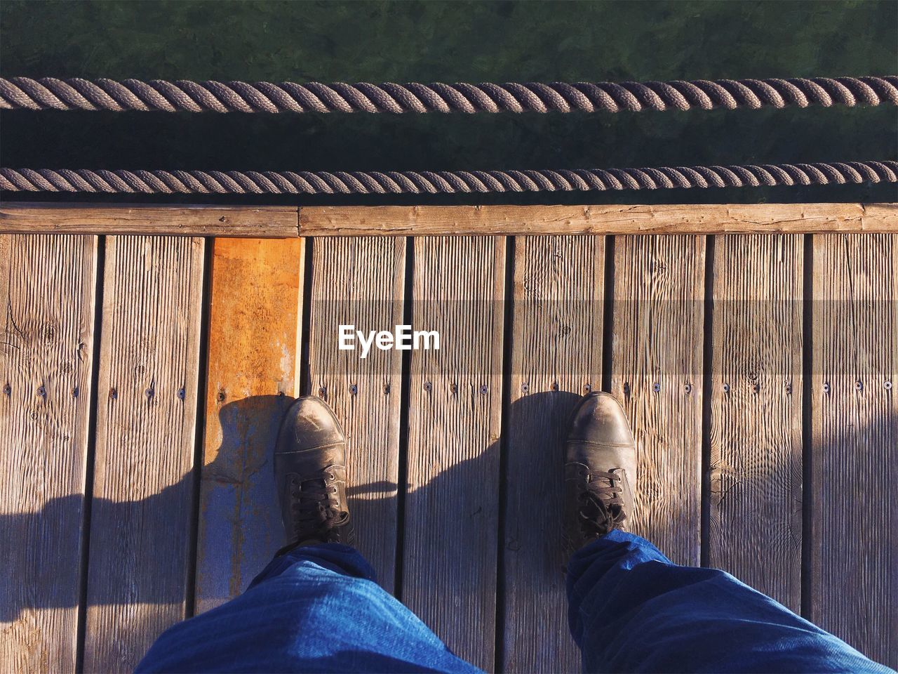 Low section of man standing on jetty by rope in sunny day