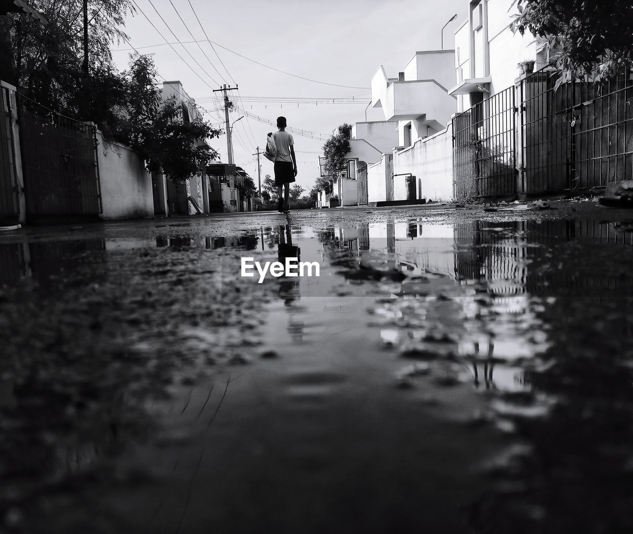 Rear view of man walking on wet road amidst buildings