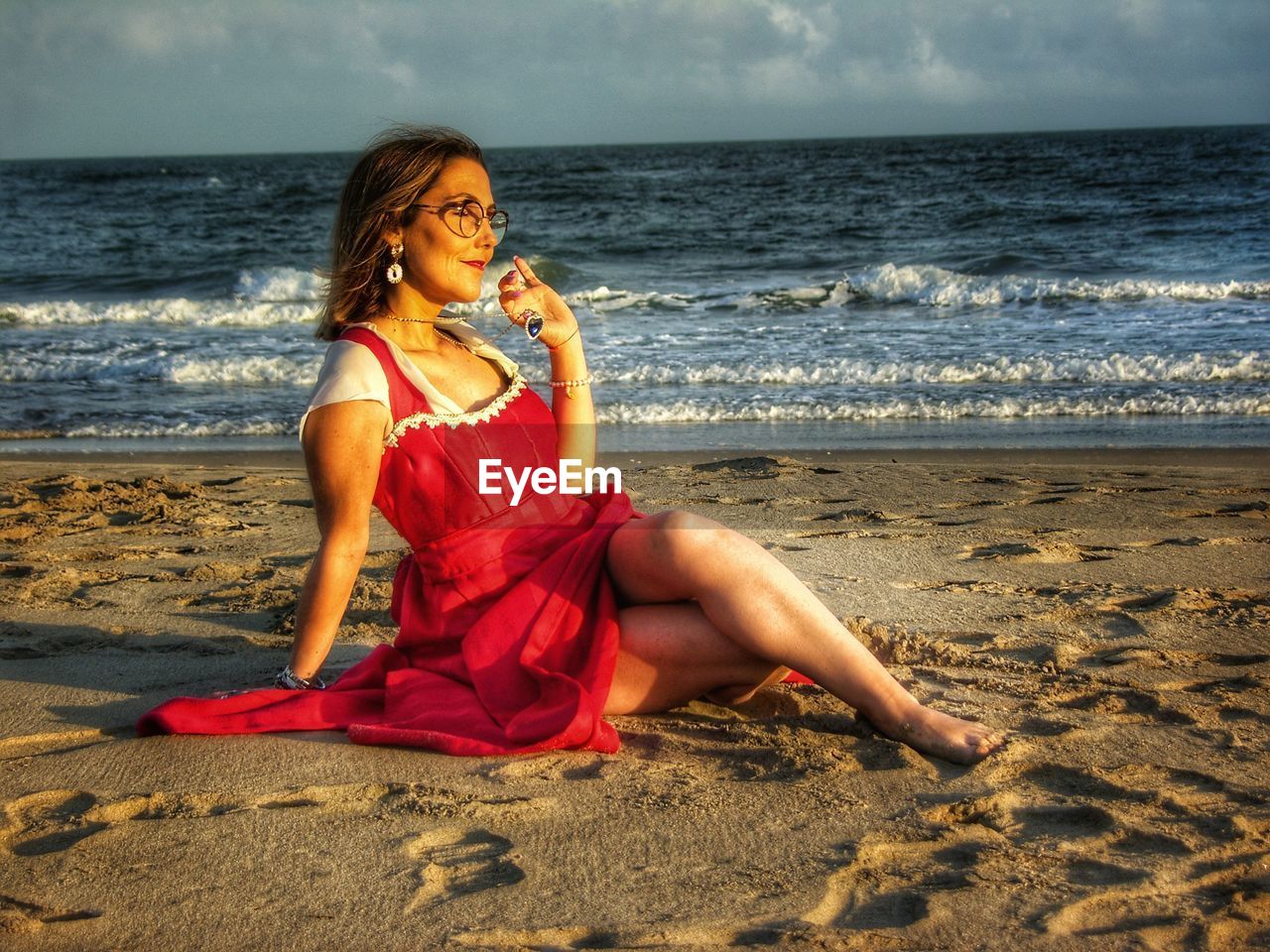 BEAUTIFUL YOUNG WOMAN SITTING ON SHORE AT BEACH