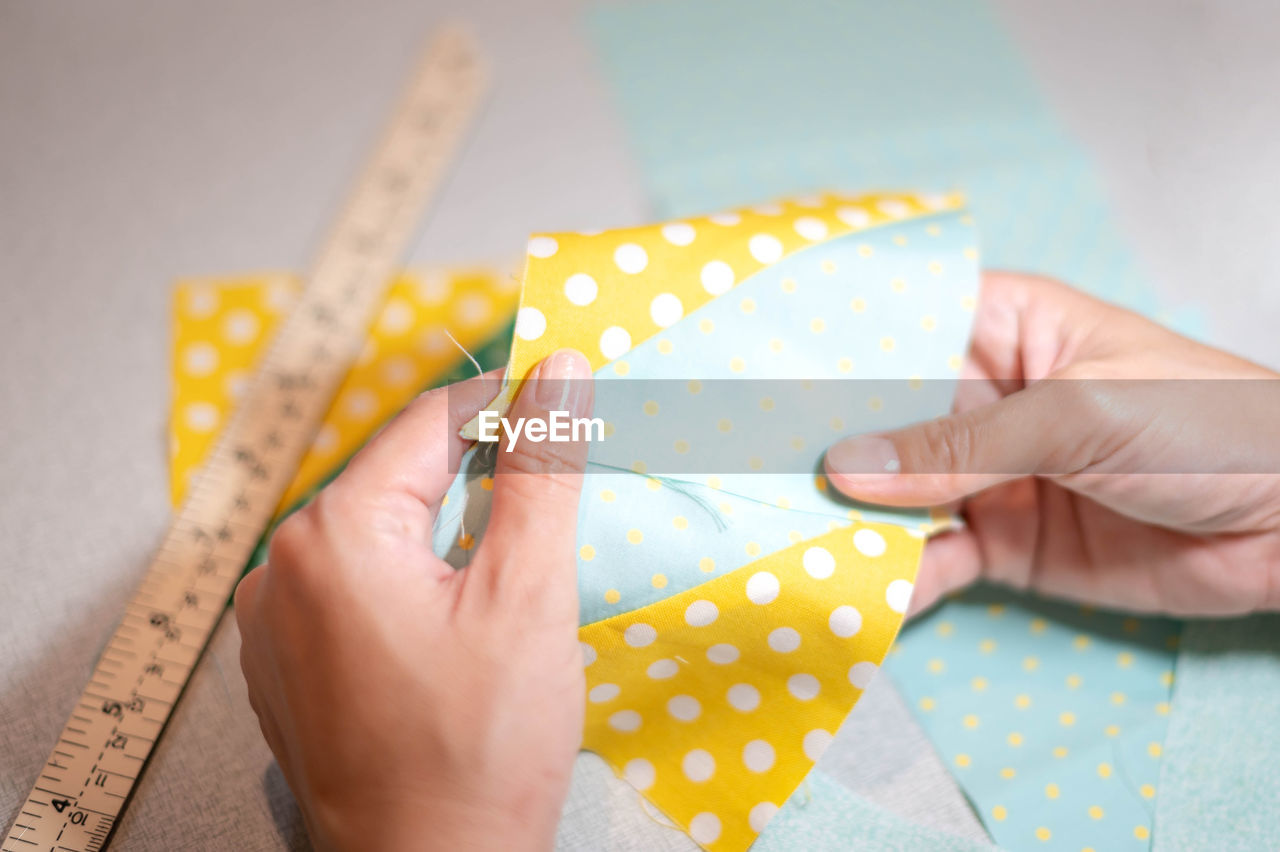 hand, one person, pattern, art, yellow, indoors, holding, adult, close-up, creativity, polka dot, textile, women, spotted, skill, craft, diy, paper, high angle view