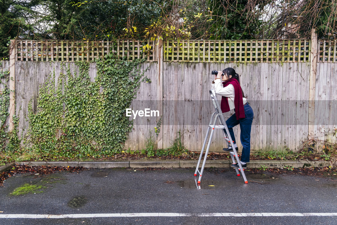Woman standing on ladder looking through binoculars
