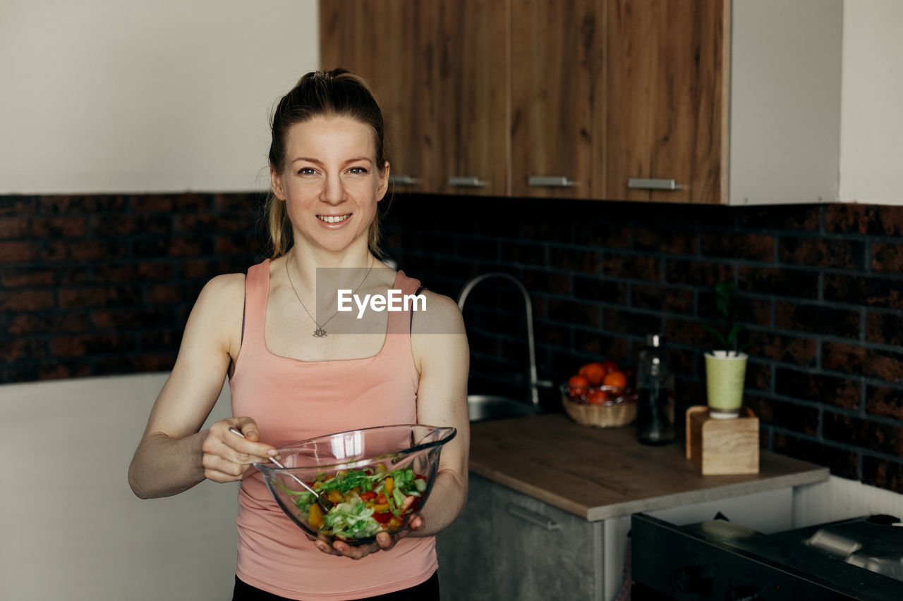 Portrait of an attractive woman holding a salad bowl and looking at the camera.