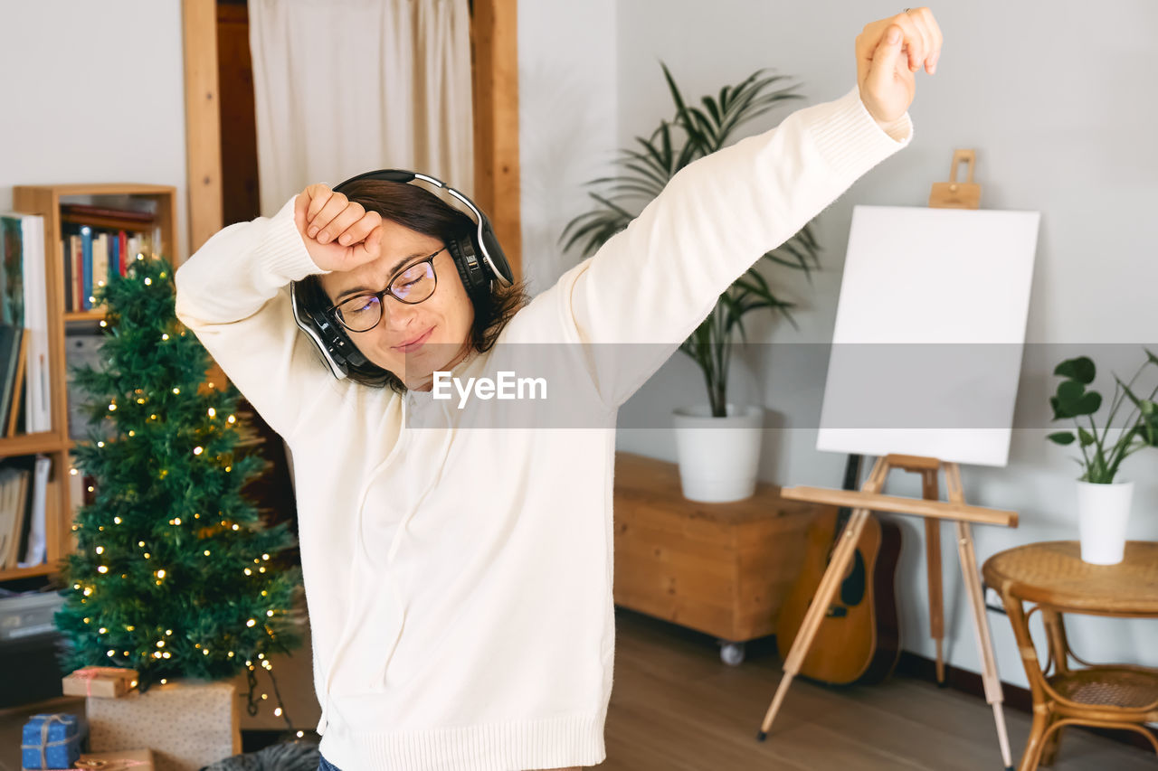 Woman listen christmas music with headphones and dancing while decorated room for christmas 