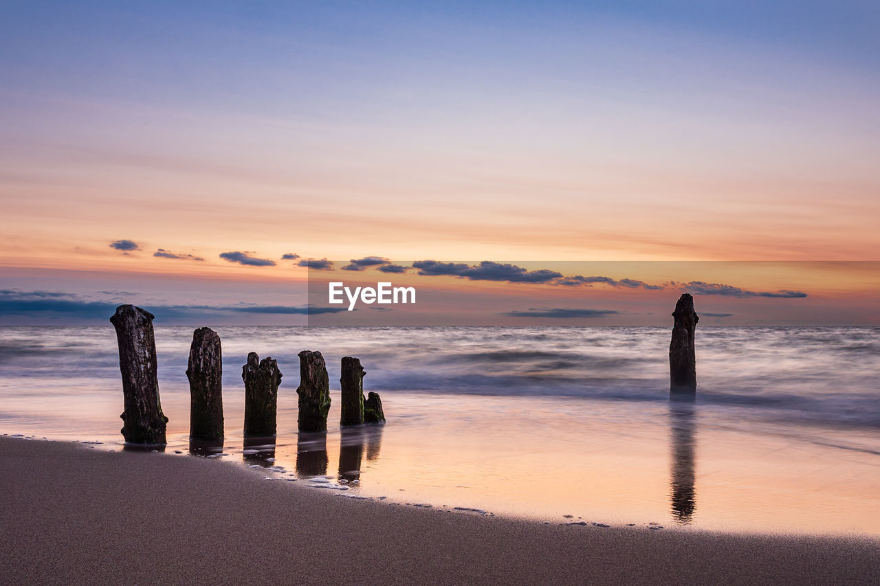 Silhouette wooden posts on beach against sky during sunset