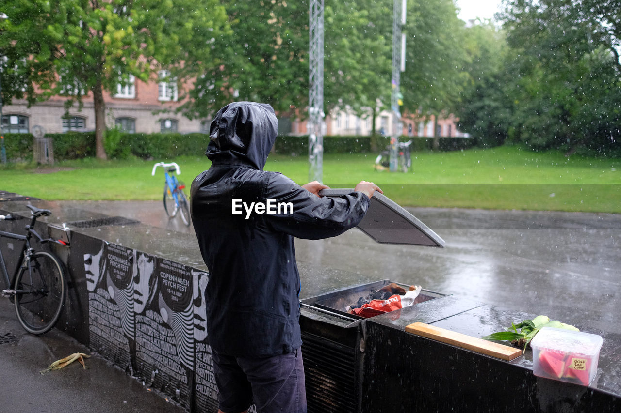 Rear view of man wearing hooded shirt preparing barbeque at yard