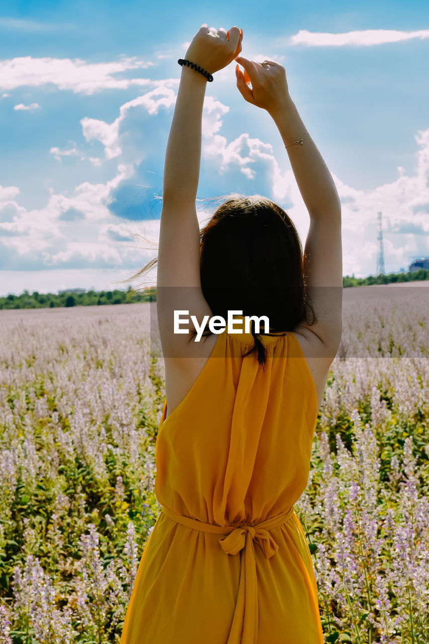 yellow, sky, one person, arm, nature, adult, arms raised, limb, cloud, women, plant, human limb, land, landscape, environment, rear view, flower, field, beauty in nature, sunlight, rural scene, young adult, waist up, summer, religion, flowering plant, tranquility, outdoors, meadow, standing, child, spirituality, female, tranquil scene, clothing, three quarter length, relaxation, lifestyles, emotion, person, day, leisure activity, idyllic, childhood, hairstyle, hand, freshness, portrait, scenics - nature, positive emotion, happiness
