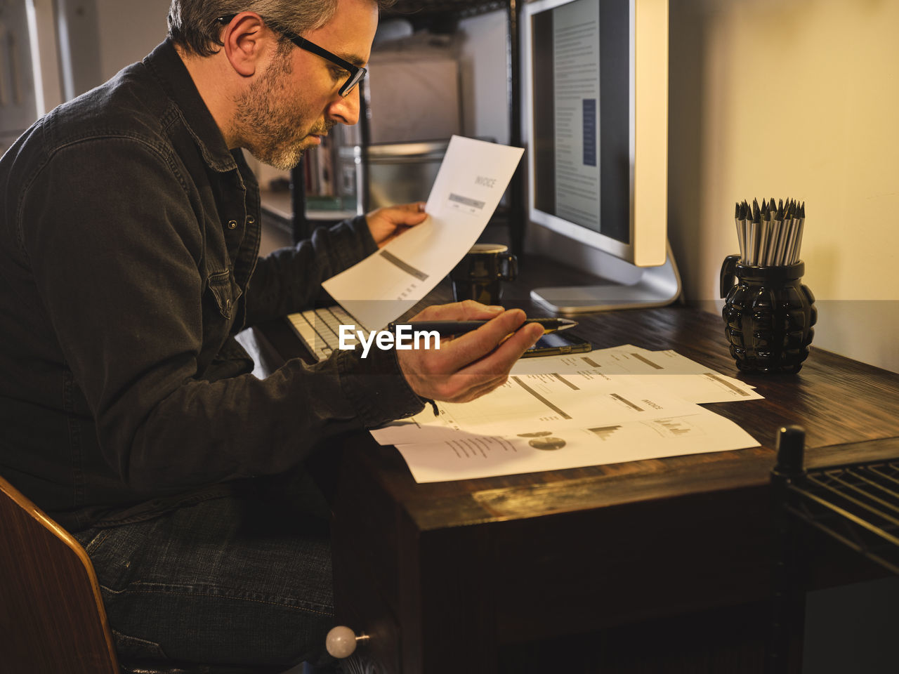 Worried and overwhelmed man at home desk with computer with notes, statistics pen and bills