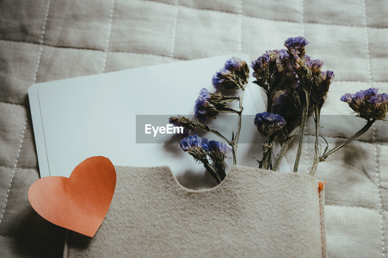 High angle view of flowers with envelope with heart shape on bed