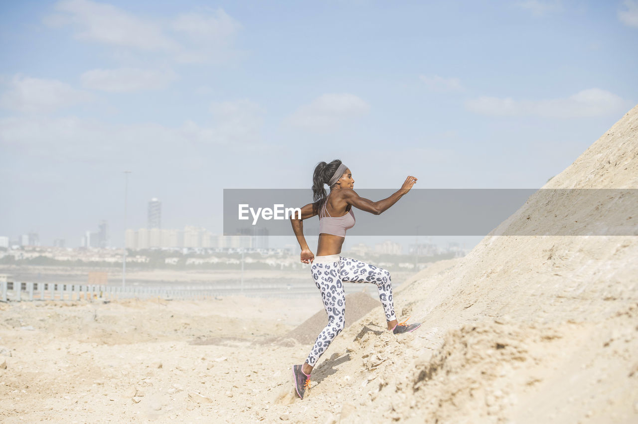 Side view of female athlete climbing rock formation against sky during sunny day