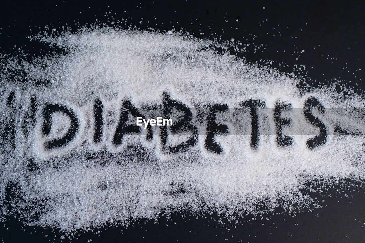 Heap of sugar with handwritten diabetes word on black background. concept of diabetes