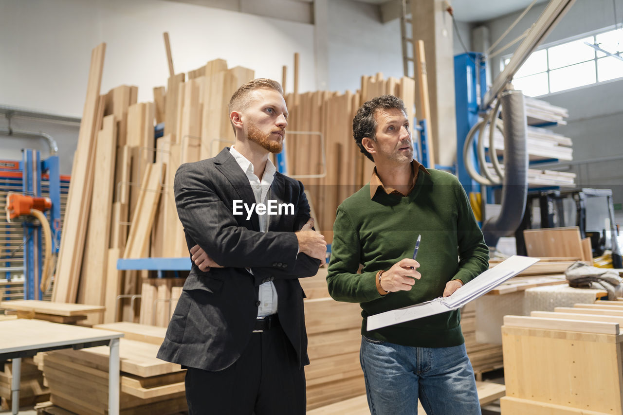 Two carpenters standing side by side and talking in production hall