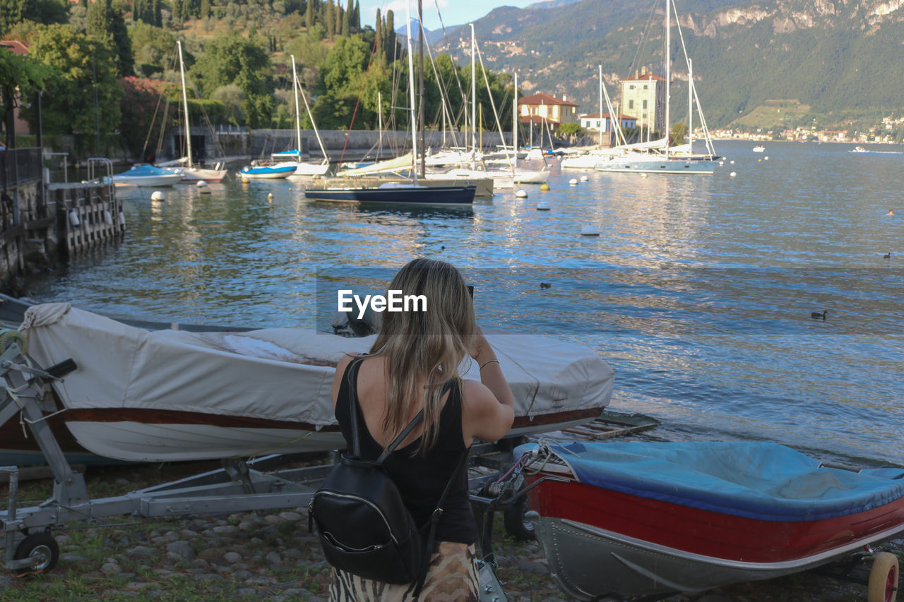 water, transportation, boat, nautical vessel, mode of transportation, one person, vehicle, nature, rear view, boating, adult, women, watercraft, leisure activity, day, sitting, vacation, lifestyles, travel, trip, ship, hairstyle, long hair, holiday, sea, tranquility, relaxation, moored, beauty in nature, outdoors, land, casual clothing, plant, blond hair, tree, beach, person, mountain, three quarter length, young adult, scenics - nature, clothing, sky, full length, travel destinations, bay, sunlight, tranquil scene, idyllic