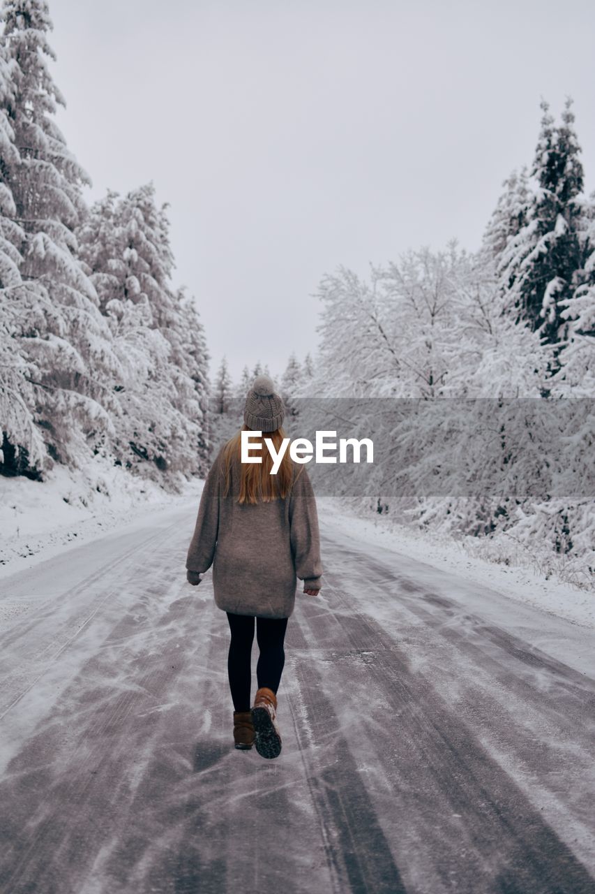 Rear view of woman walking on snow covered road