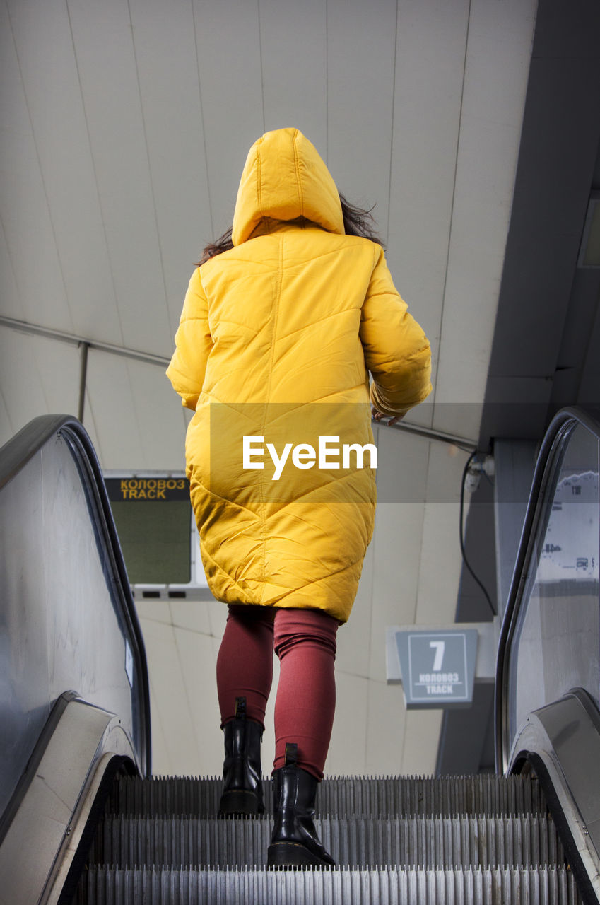 Young woman in yellow hood jacket using escalator