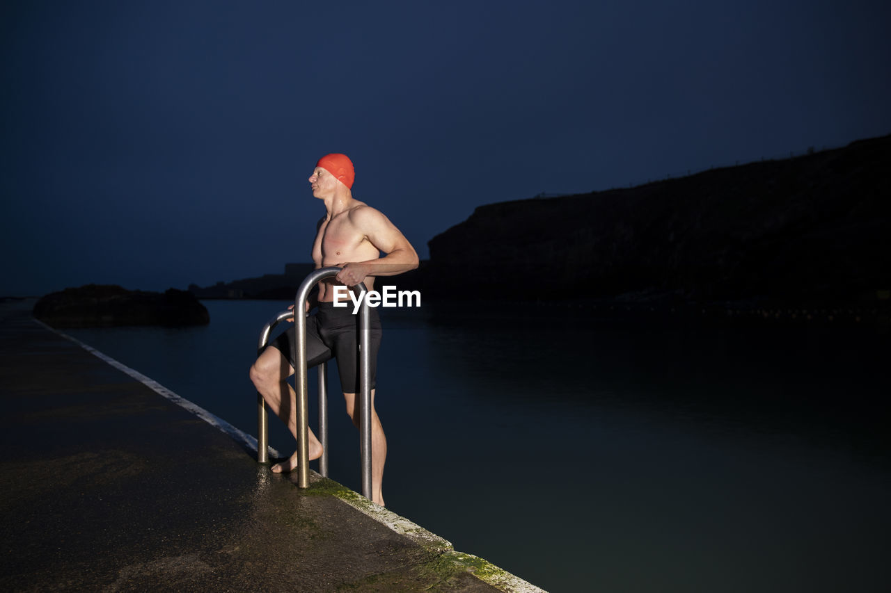 Shirtless sportsman holding railing at poolside