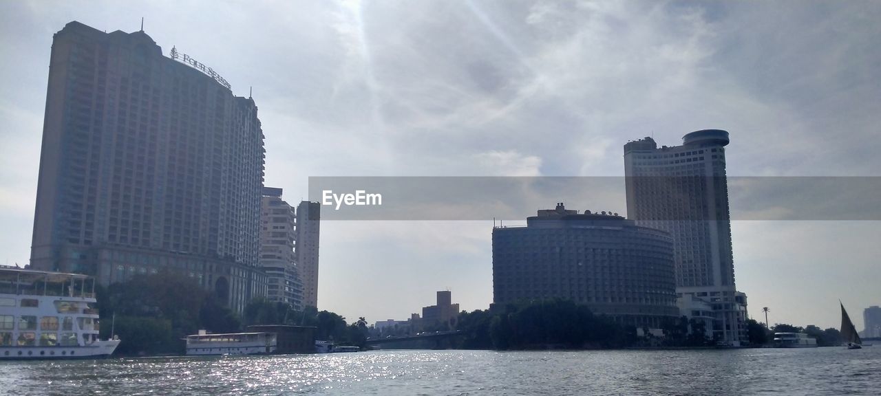 MODERN BUILDINGS BY RIVER AGAINST SKY