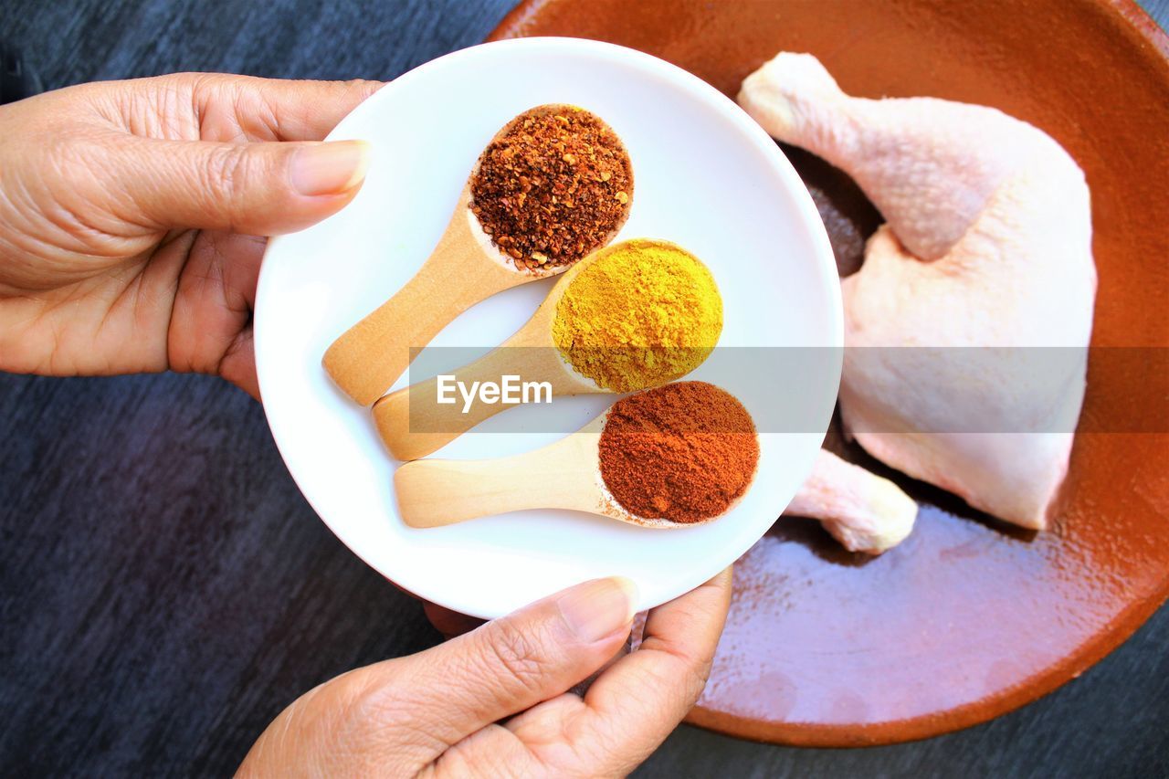 Close-up of hand holding the plate of chili pepper powder, turmeric ,and paprika in wooden spoon