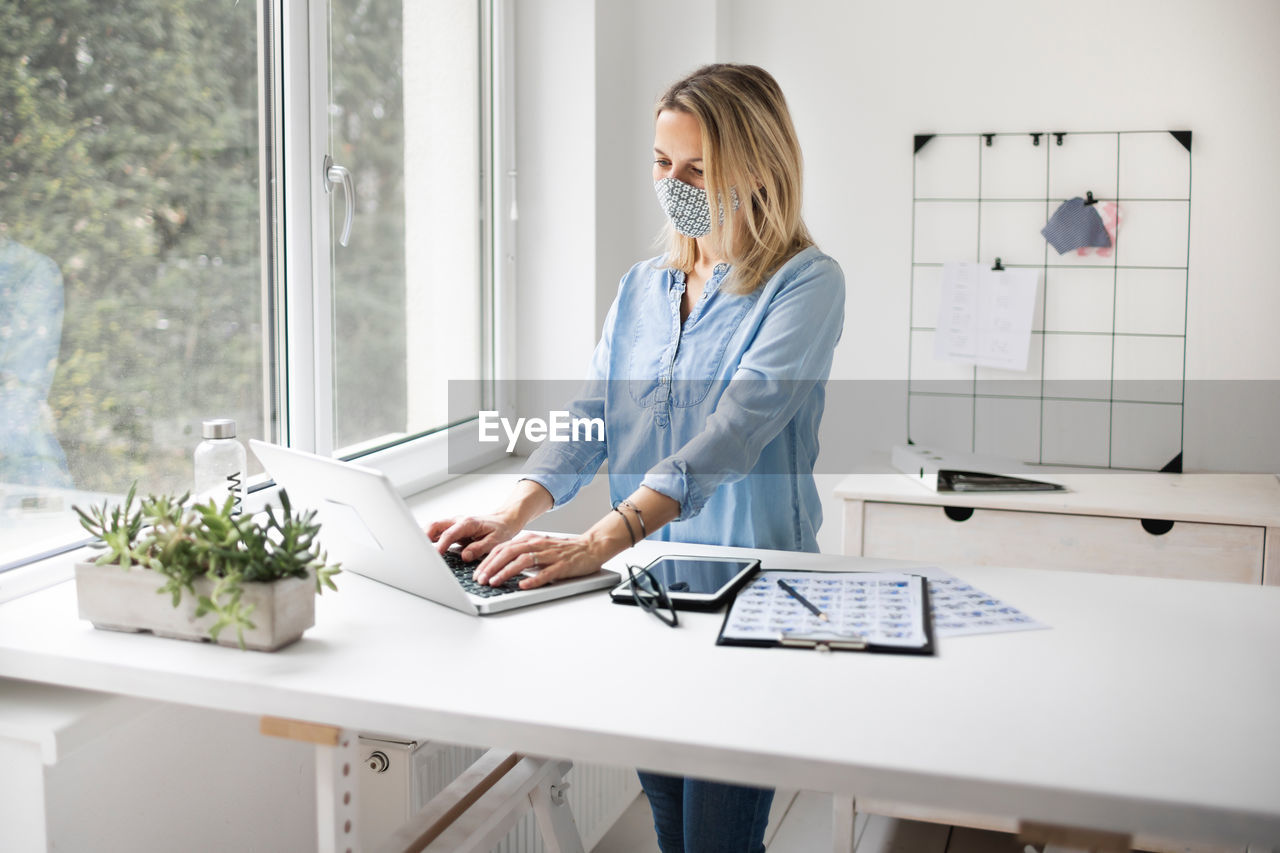 Businesswoman wearing mask while using laptop at office