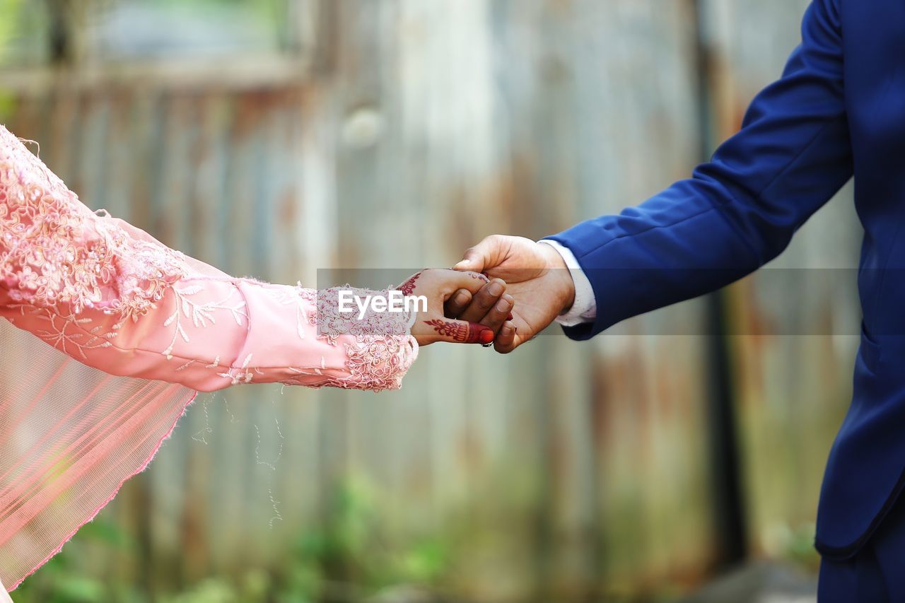 Midsection of couple holding hands while standing outdoors