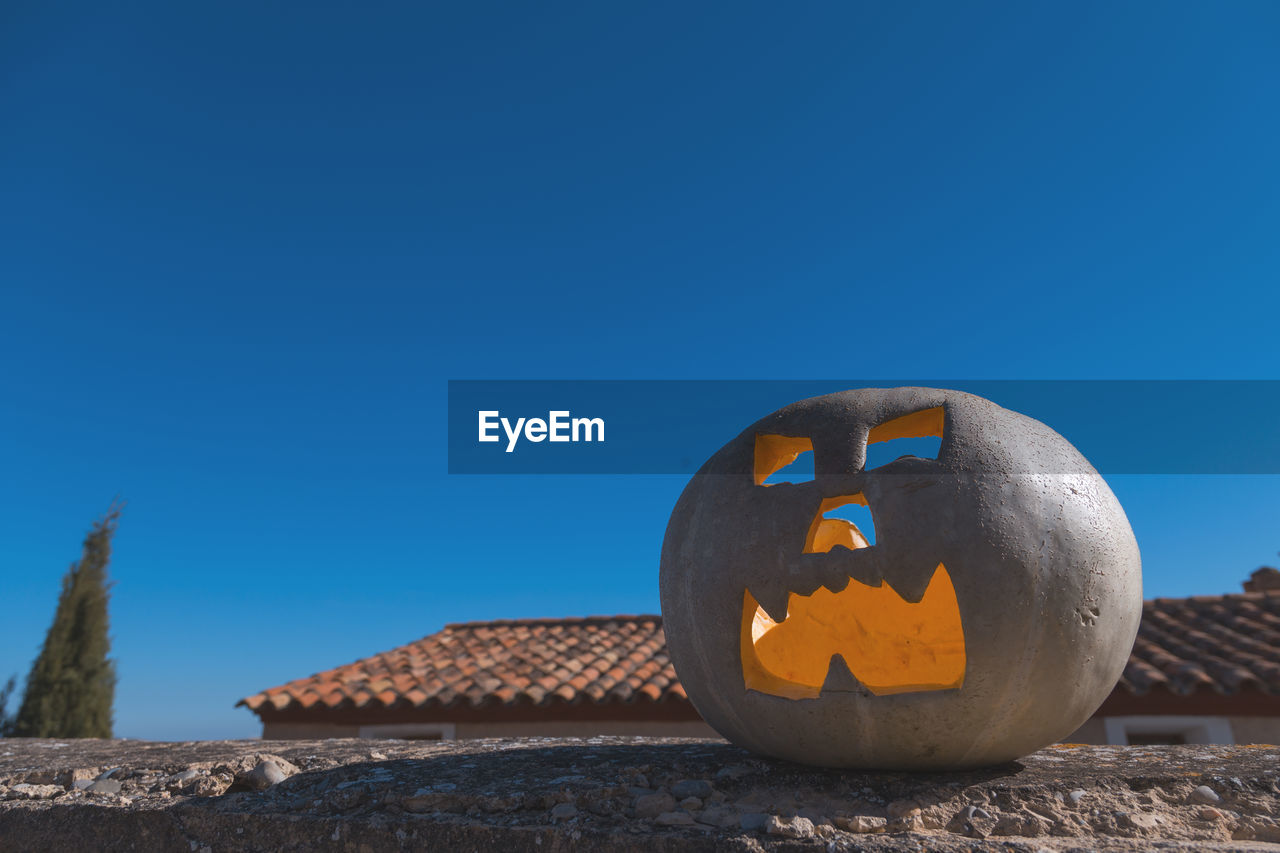 Low angle view of jack o lantern on retaining wall against clear blue sky