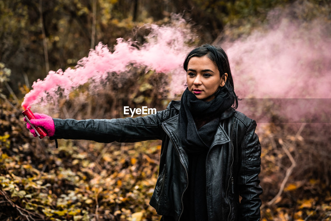 Young woman holding distress flare while standing in forest during autumn