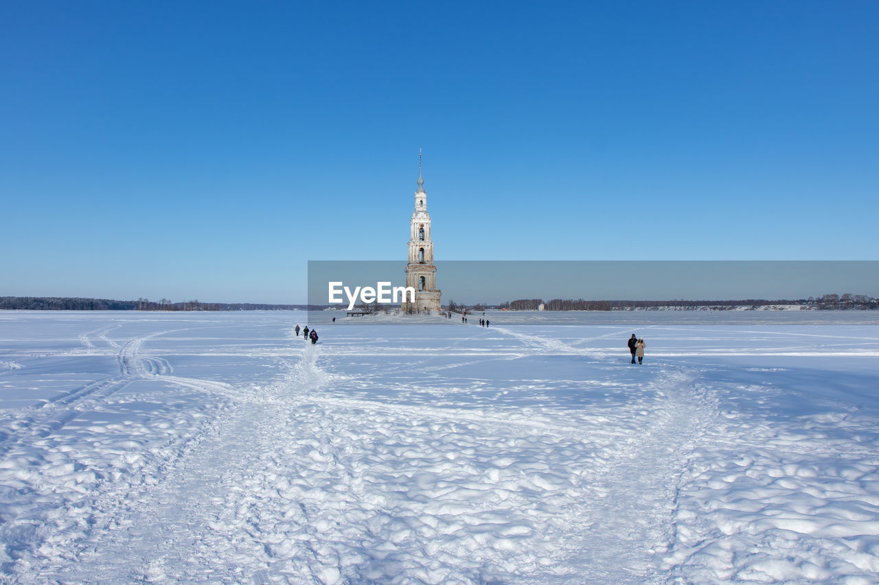 People on snow covered land against clear blue sky