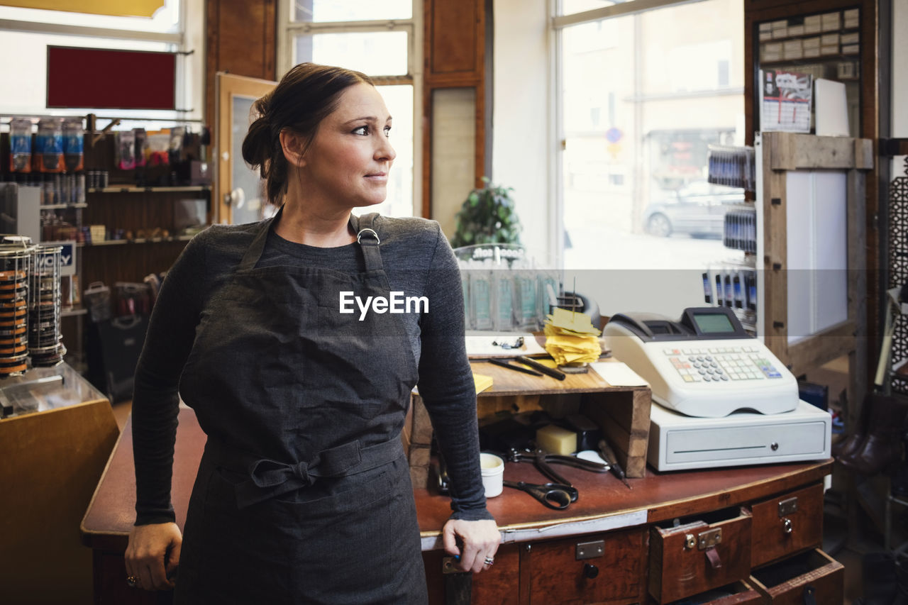 Smiling cashier standing while looking away in workshop