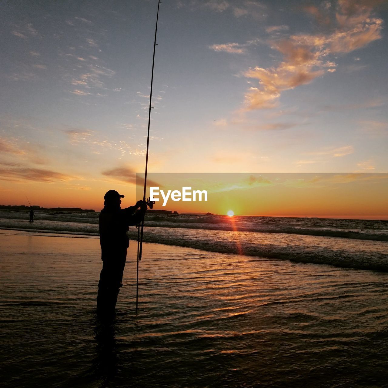 Silhouette man holding fishing rod at beach during sunset