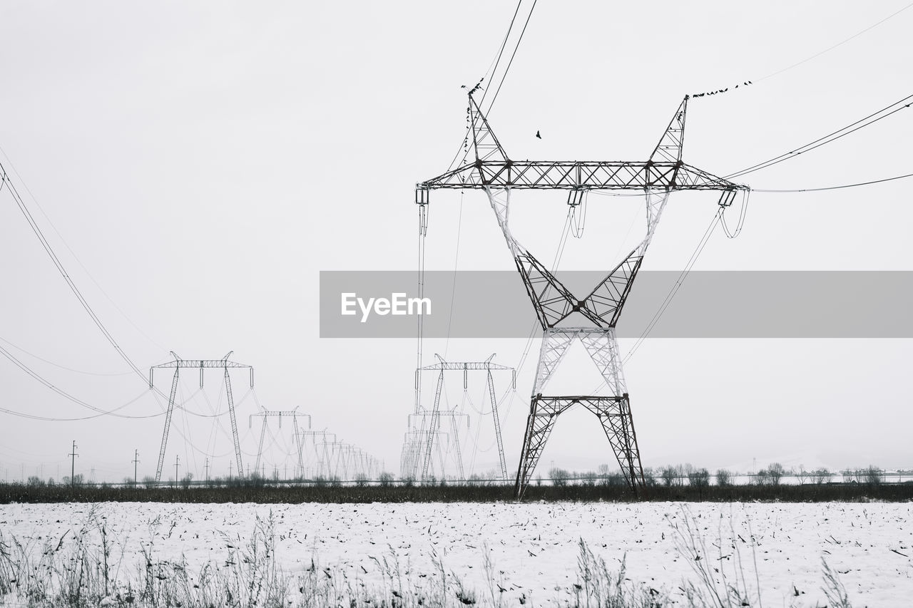 Electricity pylon on field against sky in winter